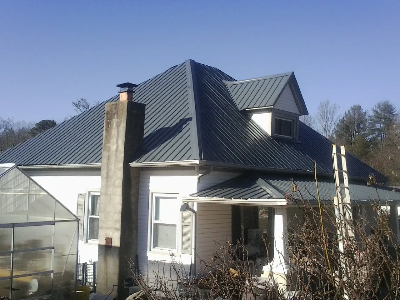 Dark blue standing seam metal roof on a white farmhouse with dormer — Slate & Tile Roof Repair by Roofing Brothers in Gattman
