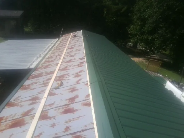 Old rusted panels beside newly installed green metal roofing — Wind Damage Roof Repair by Roofing Brothers in Gattman