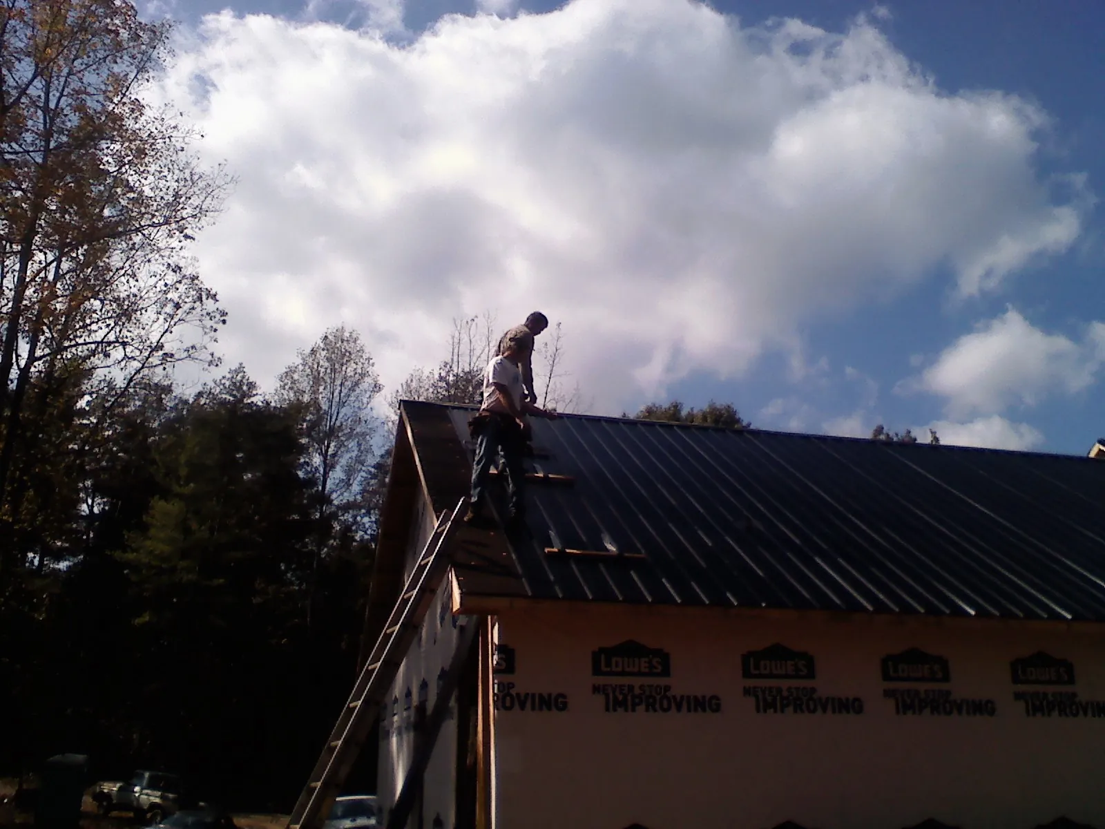 Roofer fastening dark metal panels high against a cloudy sky, from a Roof Inspection job in Gattman