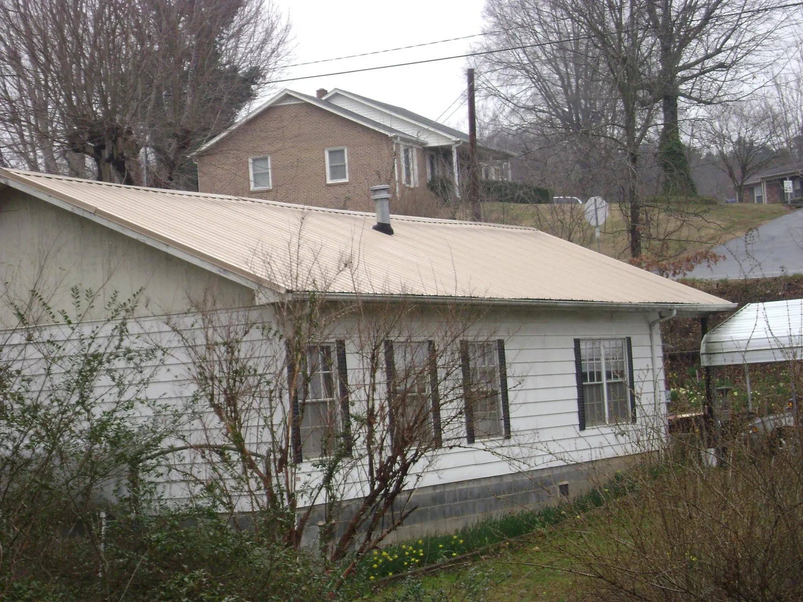 Tan metal roof on a white sided house set into a hillside — Commercial Roofing by Roofing Brothers in Gattman